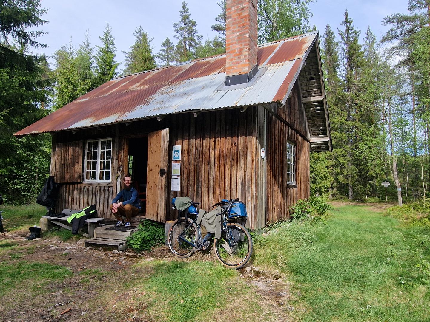 Me and my bike outside an old log building with metallic roof.