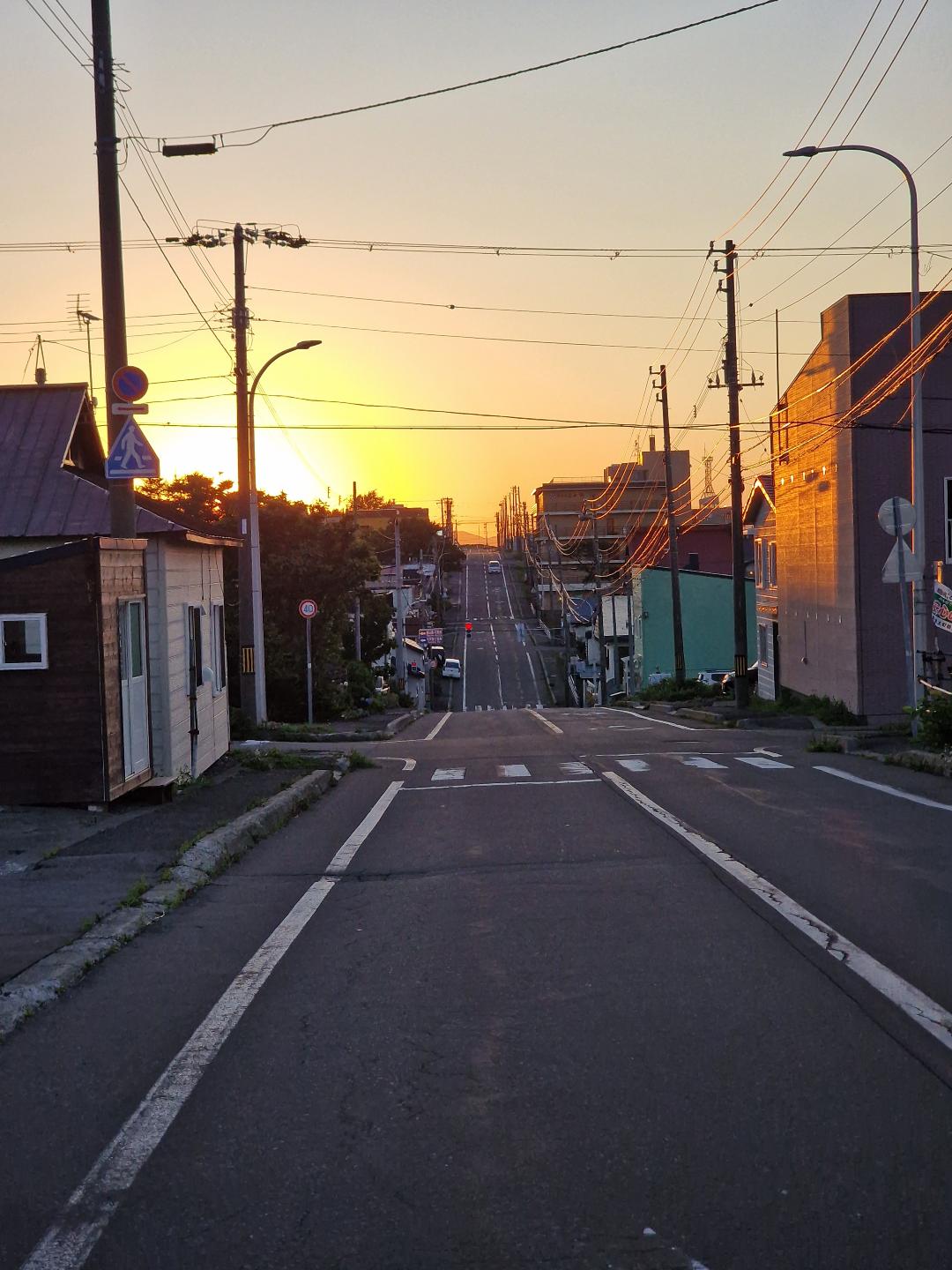 En lang rett vei, med hus på begge sider. Man ser solen gå ned. 